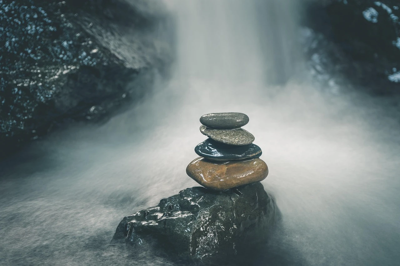 A stack of smooth stones balanced on a dark rock in the mist and spray of a waterfall.